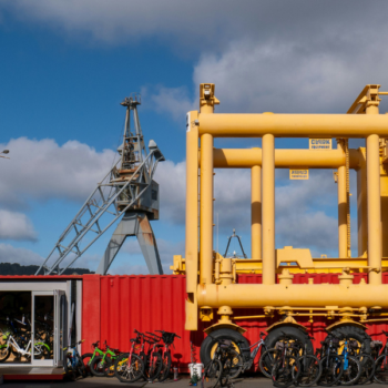 Bright yellow transport frames next to a red container with bikes, plus an industrial crane in the background.