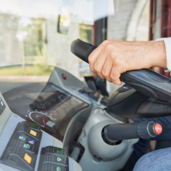 Bus driver's hand on steering wheel, dashboard visible. Technical security in verified transport.