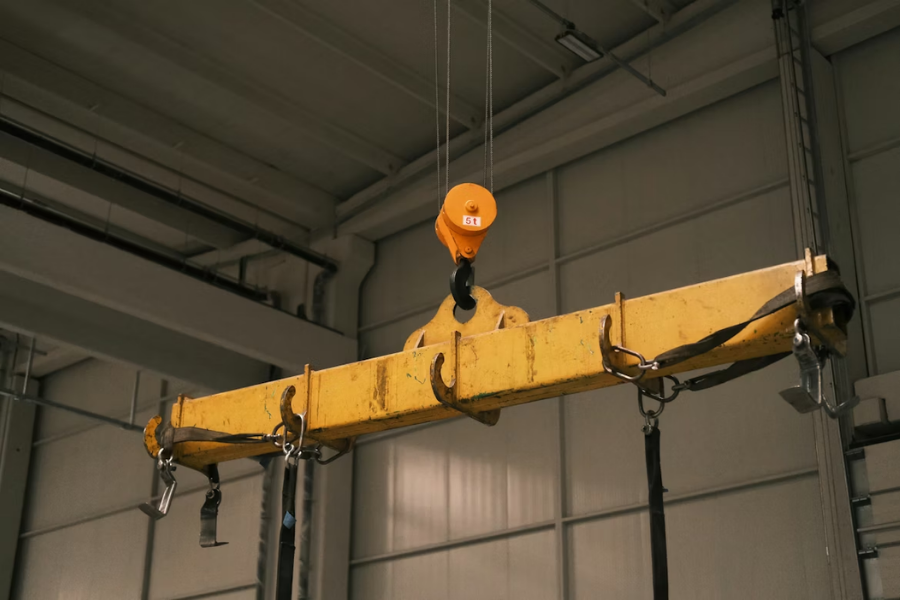 Yellow lifting beams suspended by a crane in a warehouse setting.