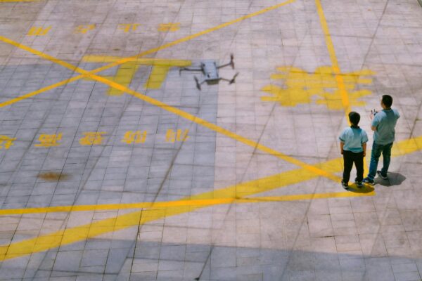 Drone hovers over a yellow-marked pad as two people observe, showcasing drone inspection for industrial asset management.