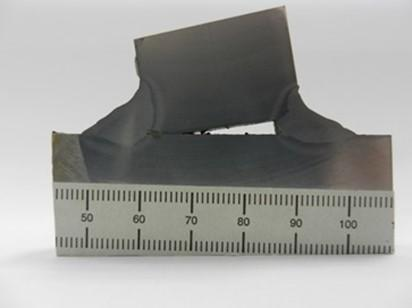 Structural integrity failure test showing deformed steel sample beside ruler.